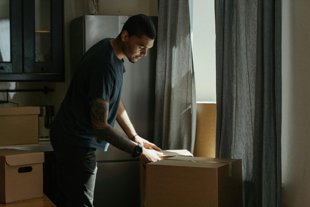 Adult man packing and unpacking boxes in a modern apartment setting.